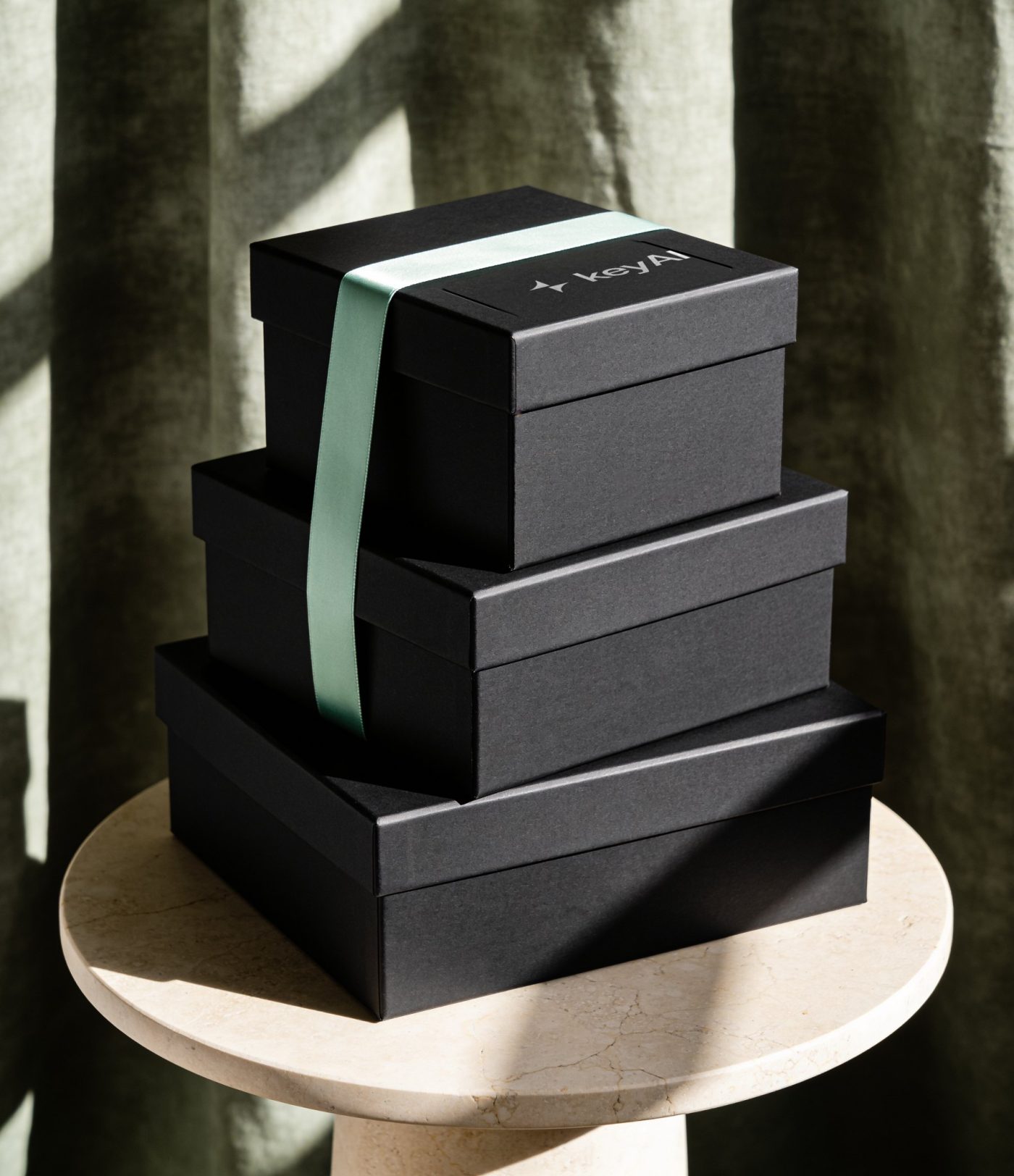 Three stacked matte black gift boxes with the white keyAI lockup and a mint ribbon
