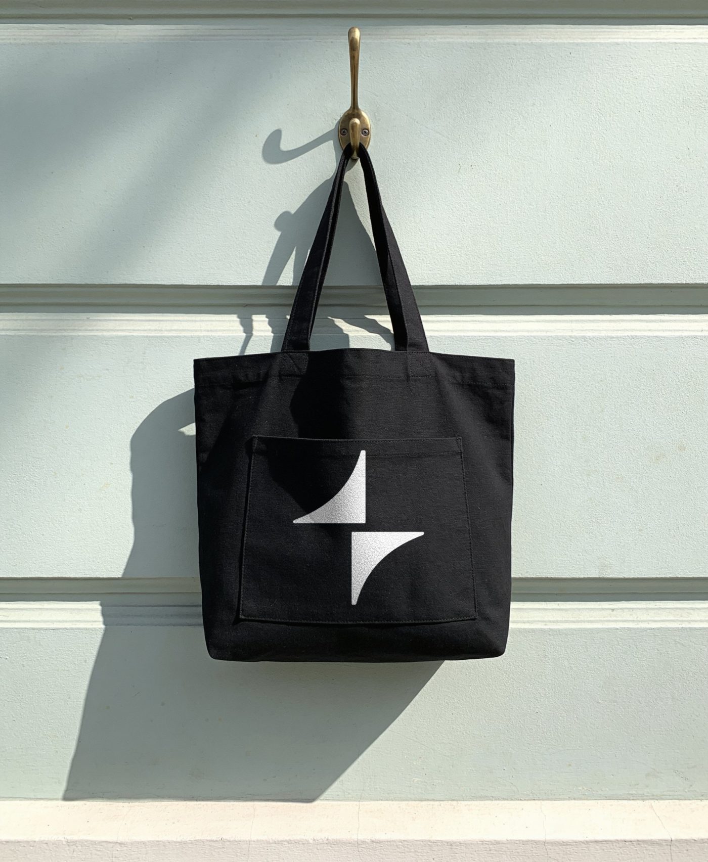 Black canvas tote on a brass hook with the white spark on its pocket
